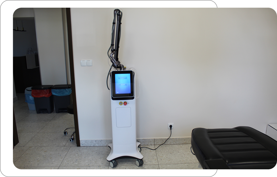 Sprzęt medyczny z ekranem dotykowym i ramieniem zabiegowym stojący w gabinecie, obok czarnego łóżka zabiegowego.