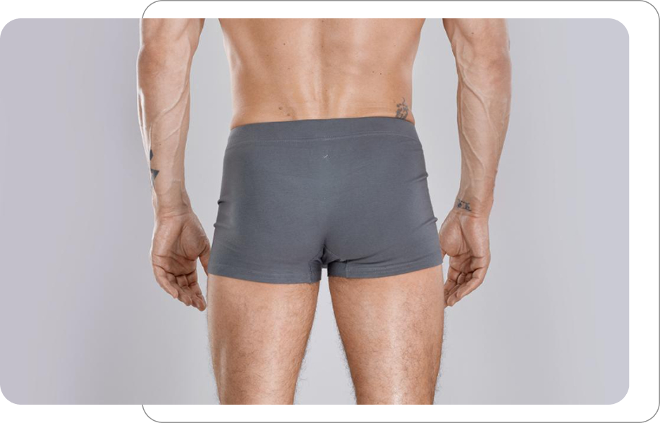 Plecy i pośladki mężczyzny w szarych bokserkach widok od tyłu jako ilustracja do zabiegów modelujących sylwetkę lub pielęgnacji męskiej skóry ciała.