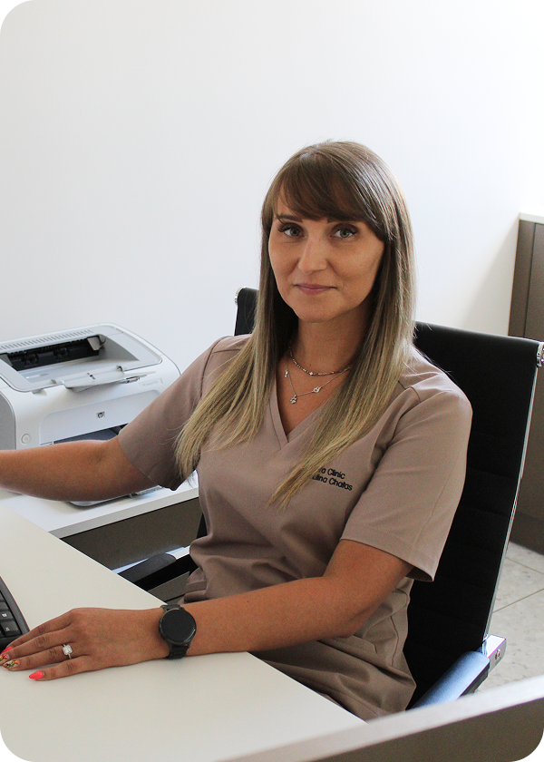 Specjalistka w uniformie medycznym siedzi przy biurku w gabinecie medycyny estetycznej.