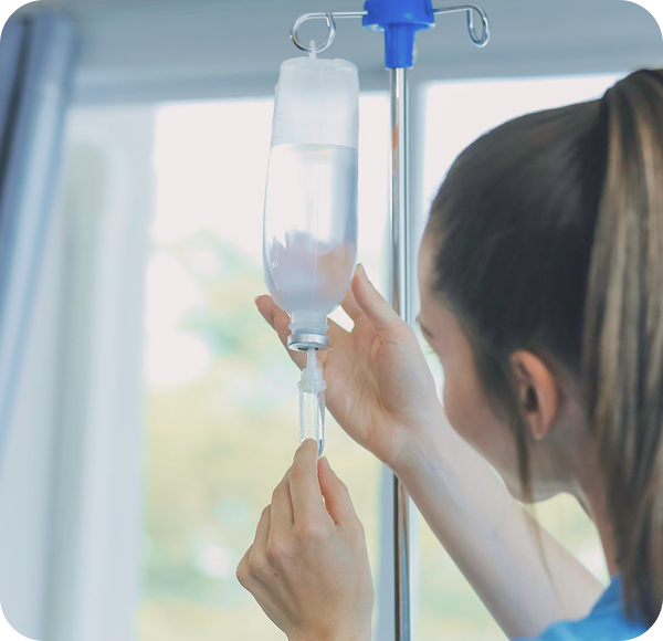 Pielęgniarka podłącza kroplówkę, regulując zestaw infuzyjny przy zawieszonej butelce z płynem.